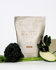 A package of KAILO Look Well collagen blend in Mixed Berry flavor, surrounded by various fruits and vegetables including mixed berries, bananas, and cucumbers.