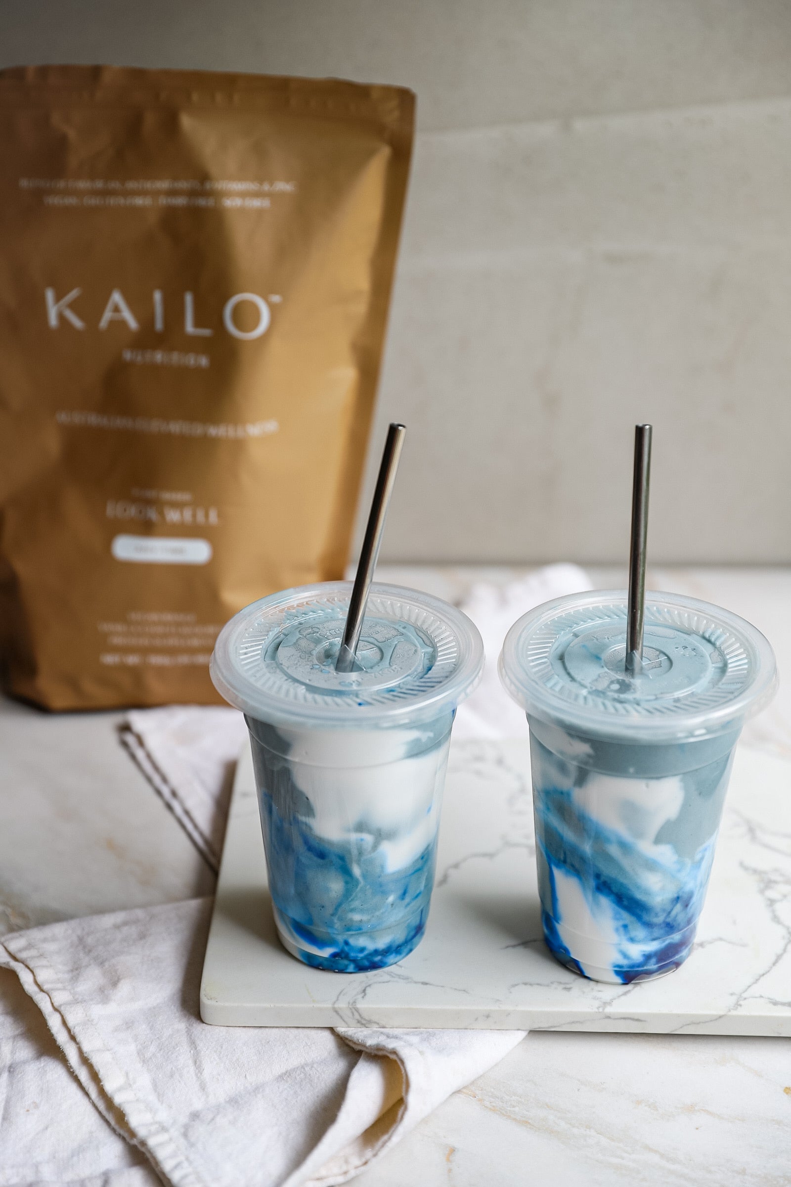 two cups of blue smoothie on a table, with KAILO Vanilla Chai bag on the background