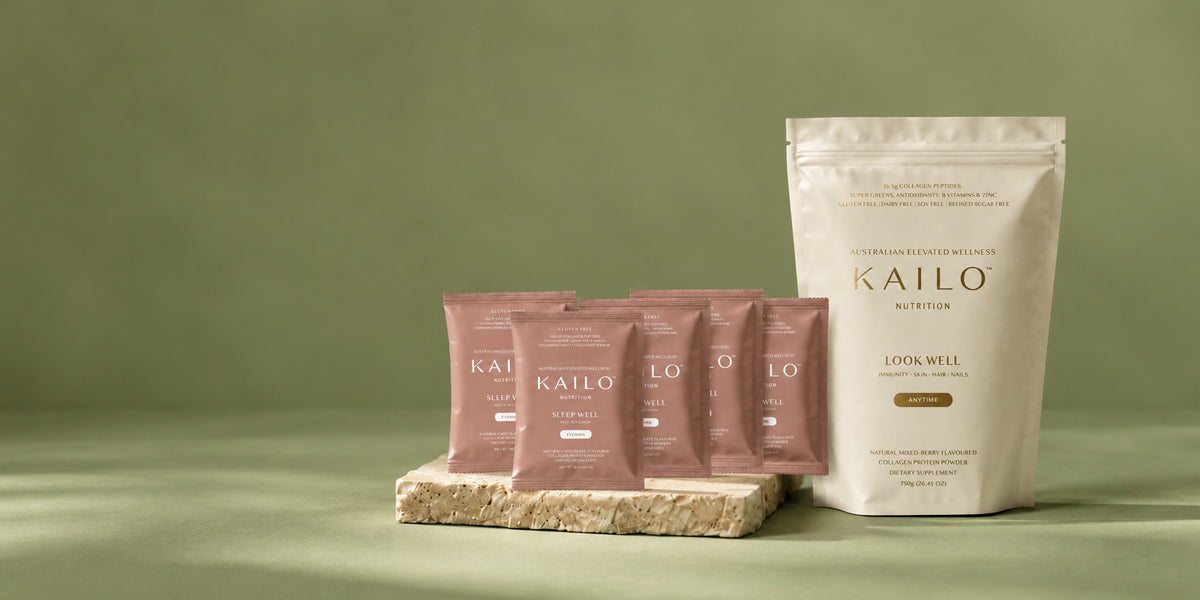 A stand-up pouch of Kailo Nutrition 'Look Well' supplement in off-white, displayed next to four smaller pink sachets arranged on a textured stone slab against a muted olive green background.