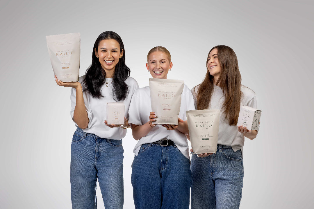 Three women holding KAILO products against a plain background