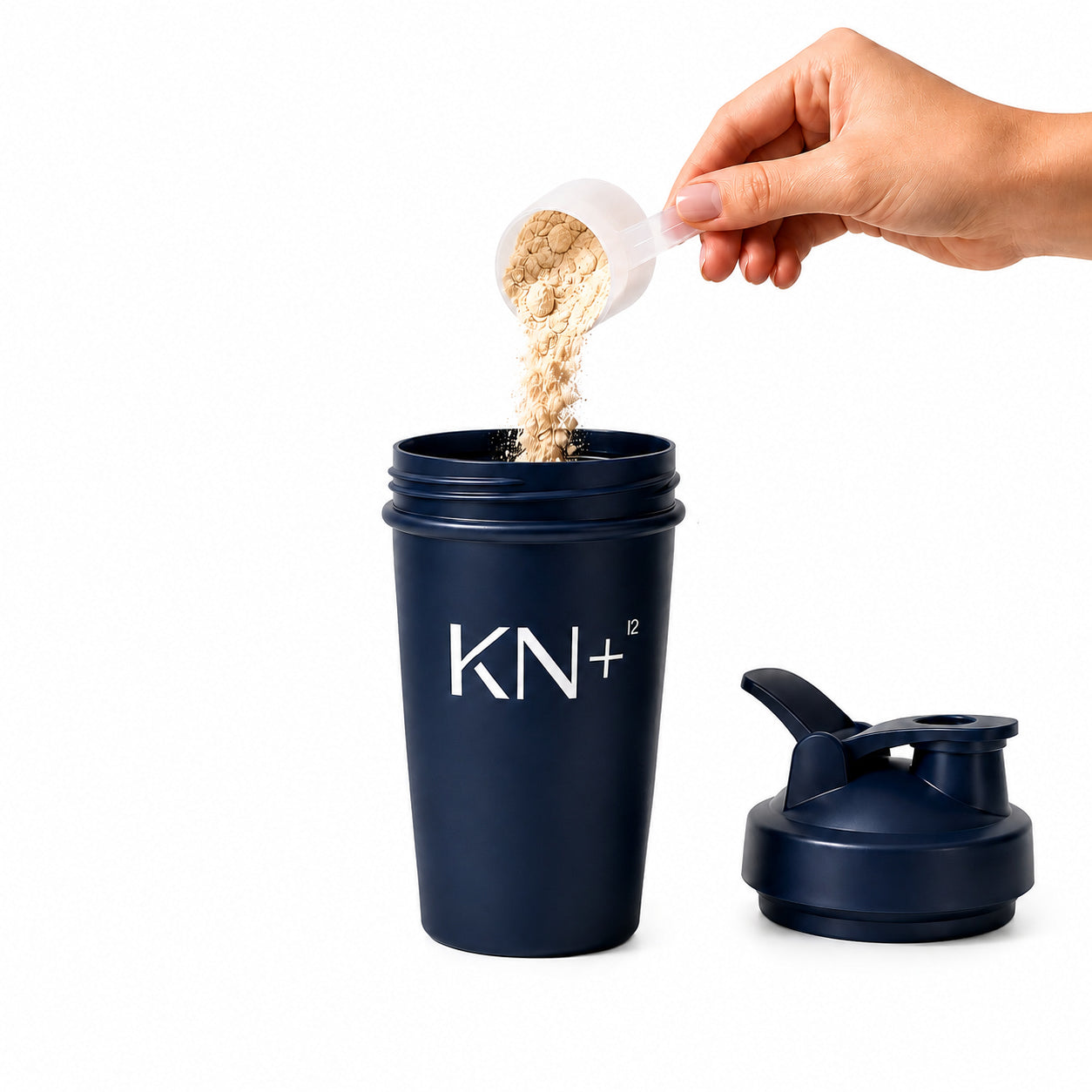 Navy blue shaker cup with 'KN+12' branding, being filled with powder from a white scoop.
