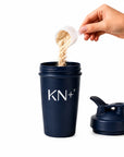Navy blue shaker cup with 'KN+12' branding, being filled with powder from a white scoop.
