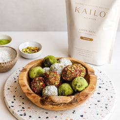 Wooden bowl with colorful energy balls on a speckled surface, Kailo Nutrition package in the background.