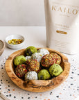 Wooden bowl with colorful energy balls on a speckled surface, Kailo Nutrition package in the background.