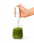 Hand holding a white milk frother with 'Kailo' branding over a glass of green liquid.