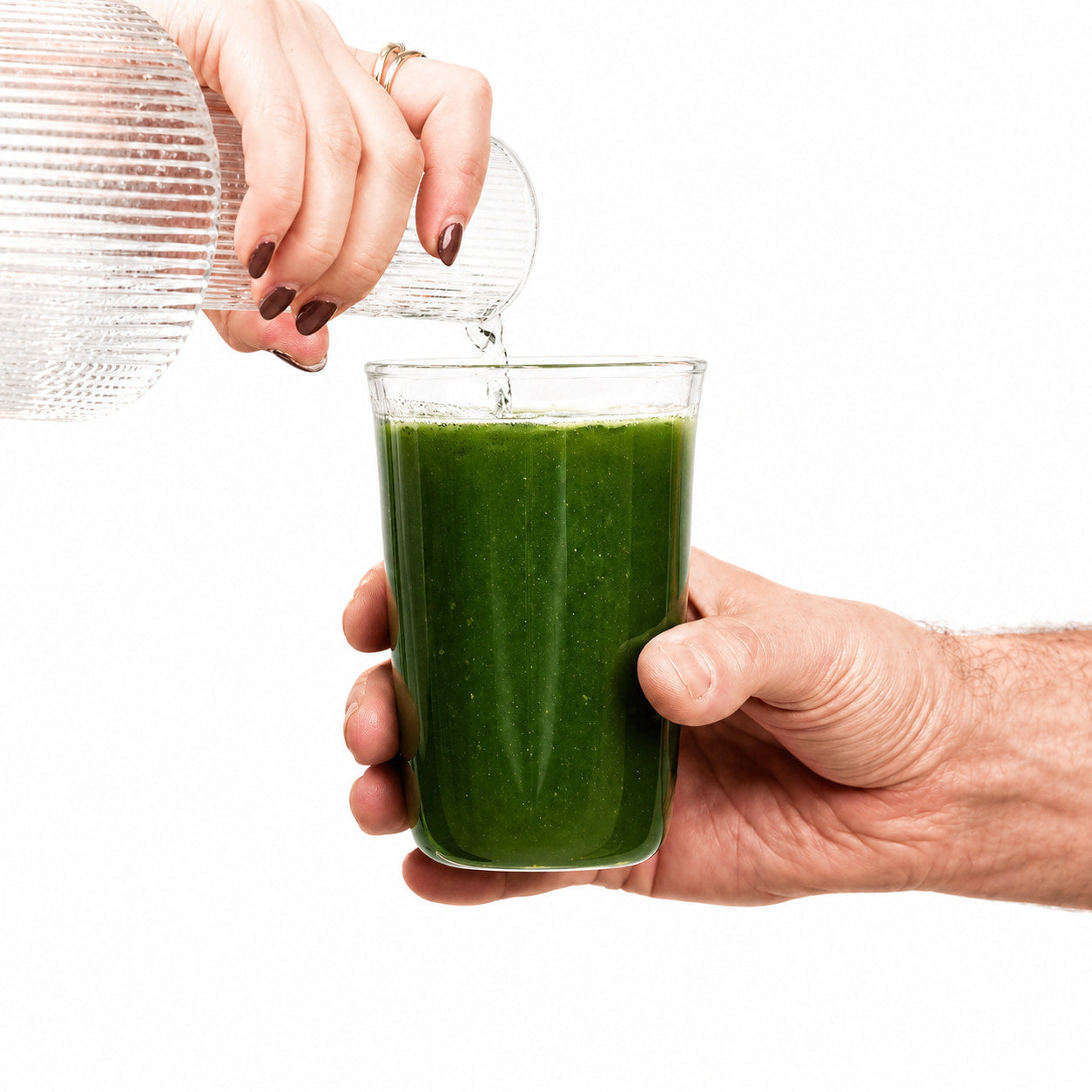 Person pouring green juice from a bottle into a glass on a white background