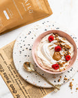 Bowl of yogurt with toppings on a plate with a newspaper underneath, next to a package labeled KAILO
