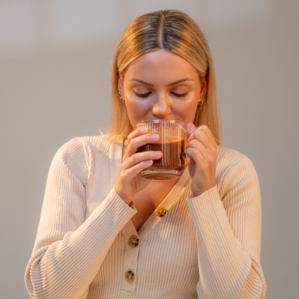 Woman drinking from a glass mug against a plain background