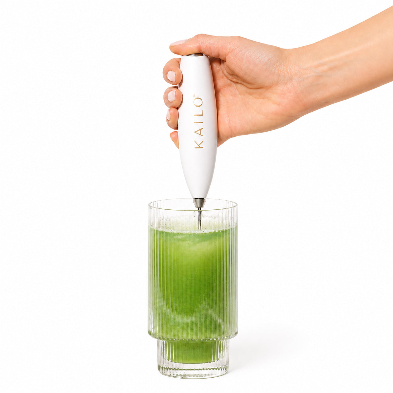 Hand using a KAILO milk frother to create foam in a glass of green liquid on a white background