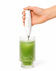 Hand using a KAILO frother  in a glass of green liquid on a white background